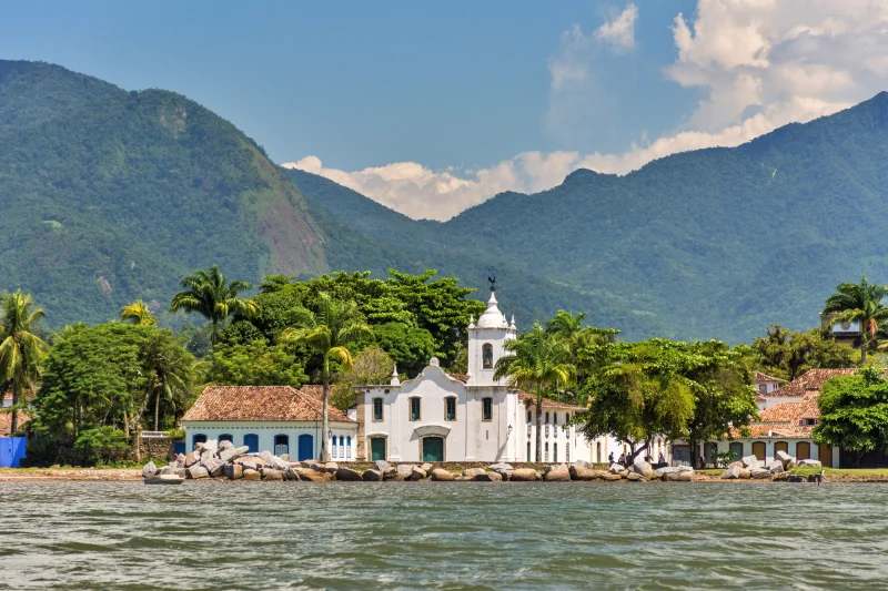 Foto do centro histórico de Paraty vista do mar, com casarios coloniais, igrejas e montanhas ao fundo — cenário clássico do litoral sul do Rio de Janeiro. Roteiro em Paraty
