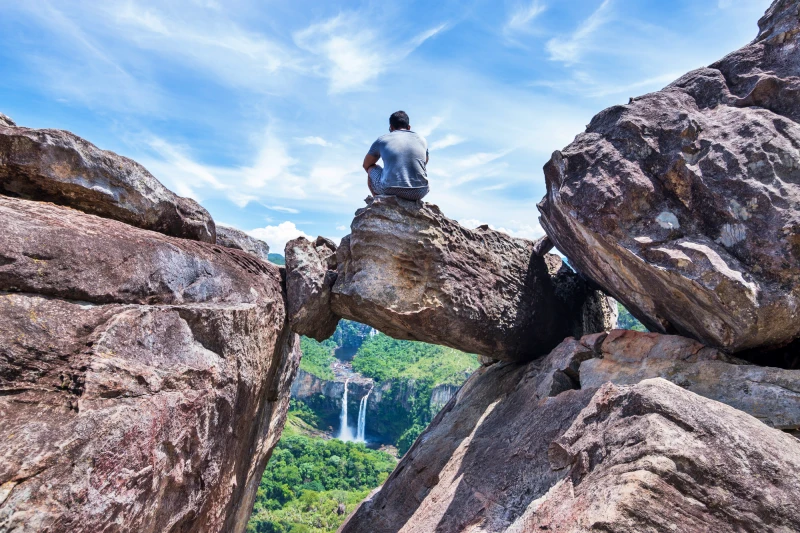 Pessoa sentada observando uma cachoeira no Parque Nacional da Chapada dos Veadeiros, um dos melhores lugares para viajar em julho no Brasil.