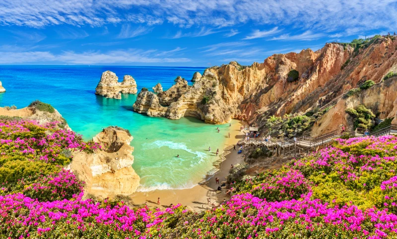 Vista da Praia do Camilo em Lagos, Algarve, com escadaria de madeira entre falésias e mar azul, representando uma viagem barata na Europa no verão