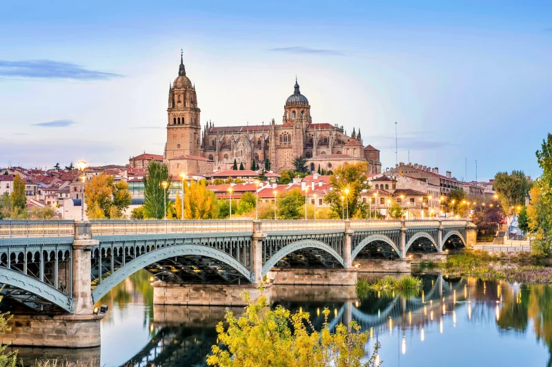 Catedral de Salamanca refletida no rio Tormes com a histórica ponte romana em primeiro plano, um dos lugares imperdíveis para conhecer na Espanha