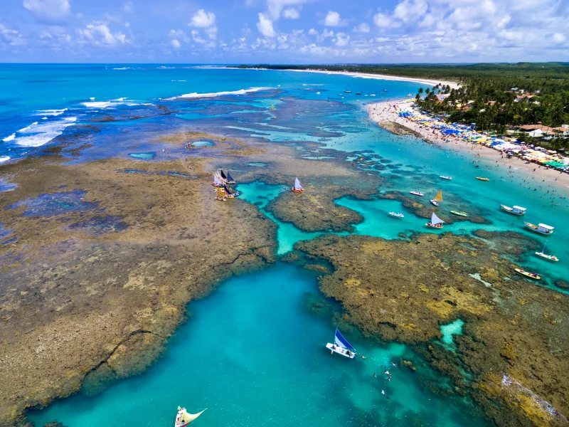 O passeio de jangada nas piscinas naturais é um dos passeios imperdíveis em Porto de Galinhas. Na foto Vista panorâmica da praia e das piscinas naturais com jangadas em Porto de Galinhas – o que fazer em Porto de Galinhas