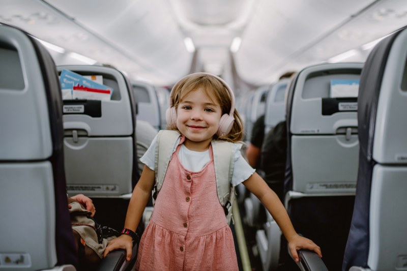 Menina sorrindo dentro de um avião durante uma viagem em família, ilustrando os documentos para viajar com crianças.