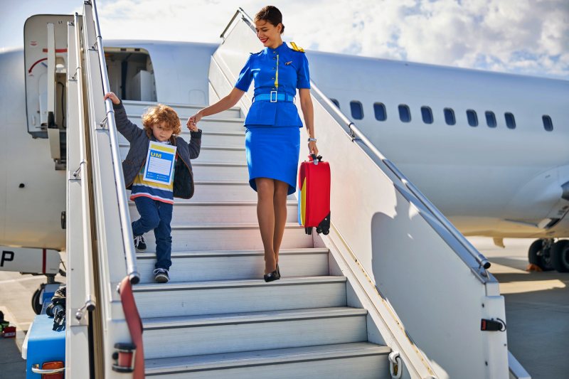 Comissária aérea acompanha uma criança durante o embarque, ilustrando os procedimentos para menor desacompanhado em viagem de avião.